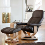 Fotografie von Stressless Sessel Consul im Wohnumfeld, Sessel und Hocker in Batick braun bezogen mit Classic Untergestell in Eichefarben gebeizt