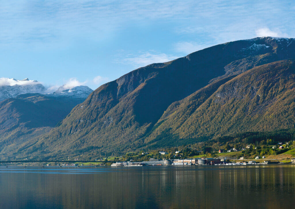 ueber-stressless-landschaft Landschaft in Norwegen, dargestellt sind Berge und ein Fjord, am Wasser liegt die Fabrik von Stressless